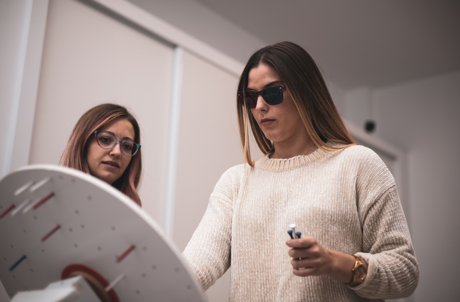 A young patient performs vision therapy tasks with her eye doctor in a dim room, wearing specialty glasses.