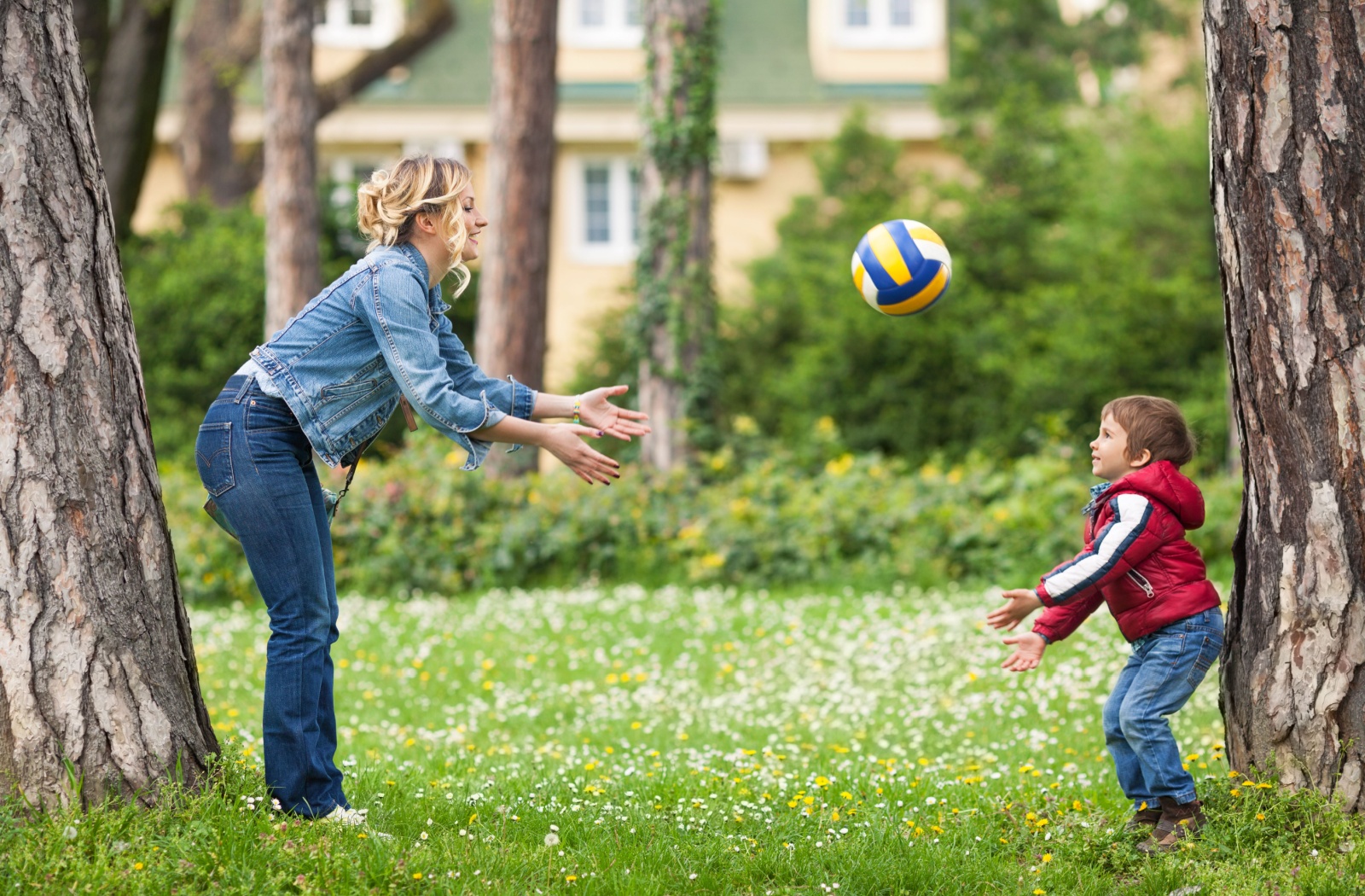 A parent and their young child at the park outside playing catch with a volleyball practicing eye-hand coordination