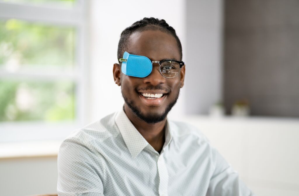 A smiling adult with a blue eyepatch over one of their eyeglasses lenses as a treatment for amblyopia or lazy eye