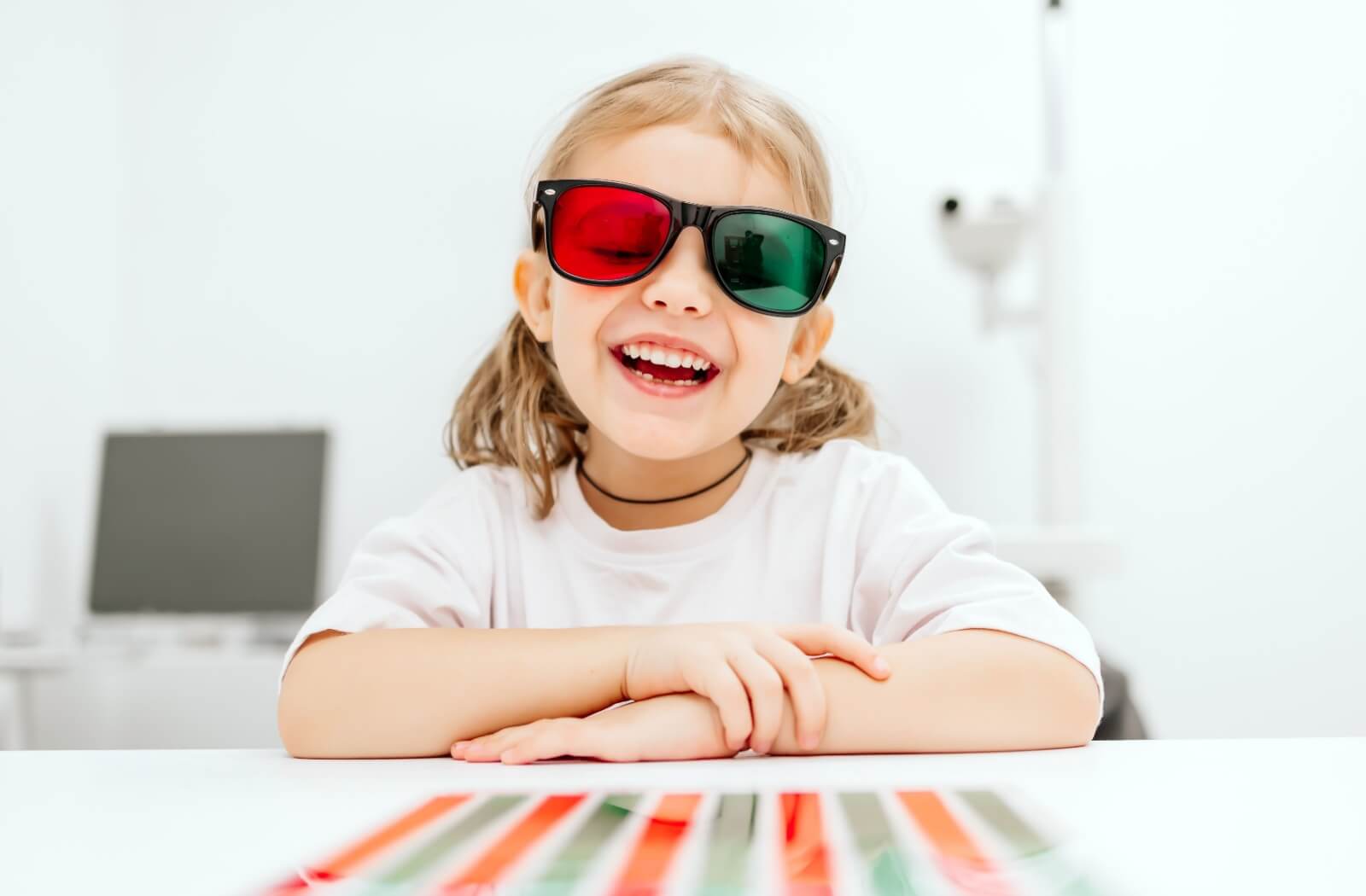 A smiling young child wears red-green glasses as part of a vision therapy exercise at a vision therapy clinic